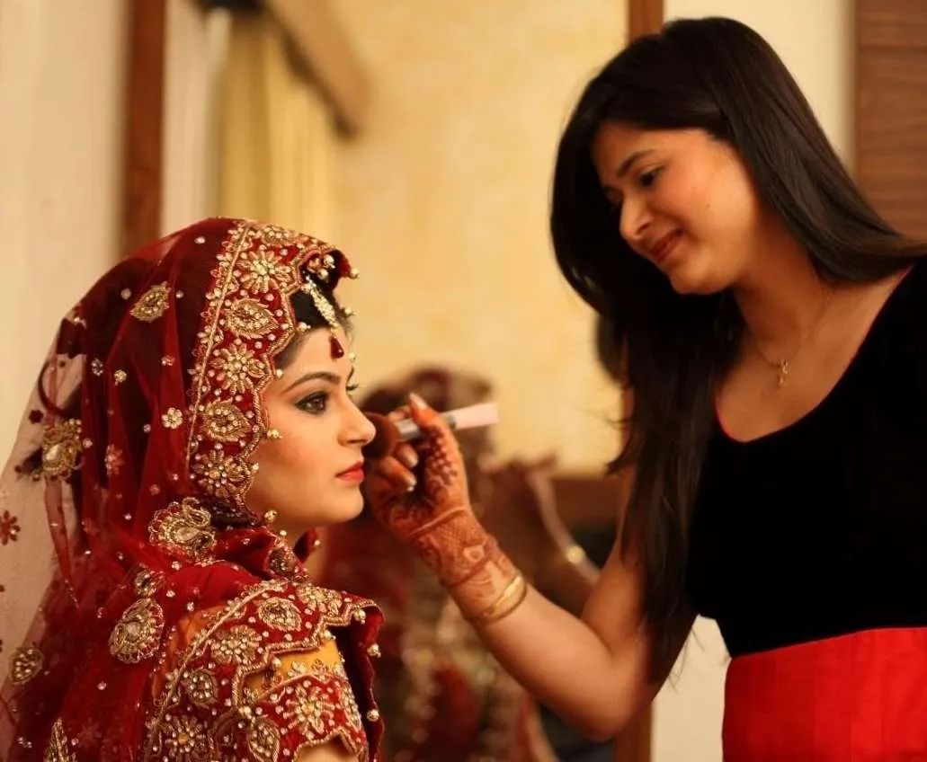 Isha, Indian bridal makeup artist in Greenville SC, applying airbrush makeup to a bride in red bridal lehenga